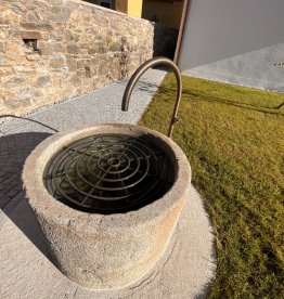 Antico mastello in pietra per crauti convertito in fontana da giardino con rubinetto in ottone e griglia per innaffiatoio all'aperto. | © ©Gasser Naturstein