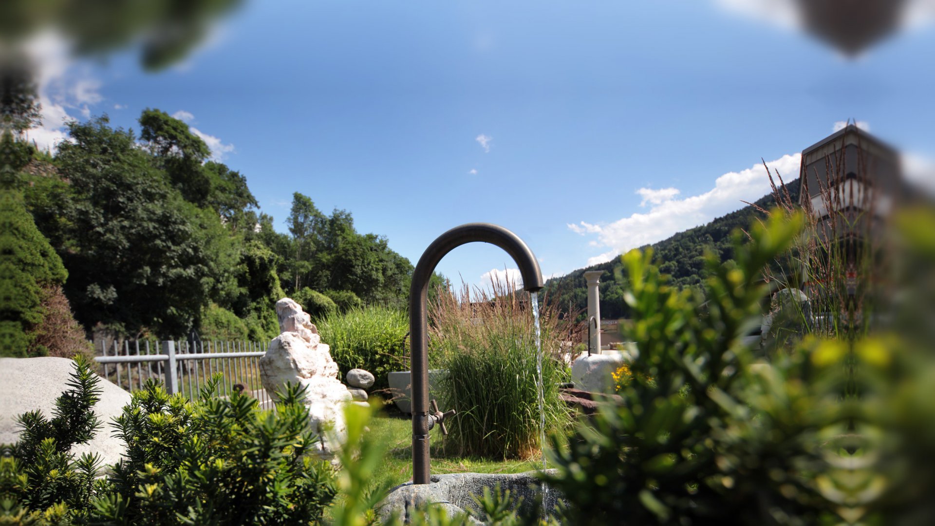 Rundbogen-Wasserhahn aus Messing über einem Steintrog mit Pampasgras – Gartenwasserhahn aus Südtirol