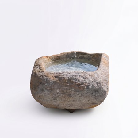 Natursteinbrunnen aus einem ausgehöhlten Granit-Findling als rustikale Wasserstelle im Garten