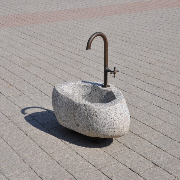 Natursteinbrunnen aus einem ausgehöhlten Granit-Findling als rustikale Wasserstelle im Garten