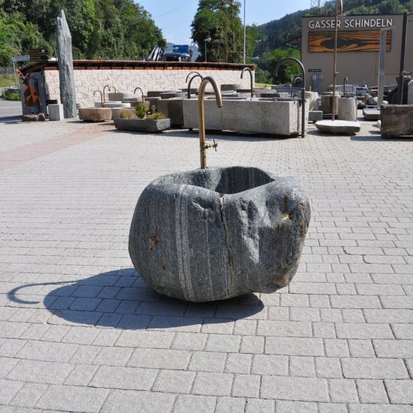 Gasser Natursteinbrunnen, Südtirol. Natursteinbrunnen aus einem ausgehöhlten Granit-Findling als rustikale Wasserstelle im Garten