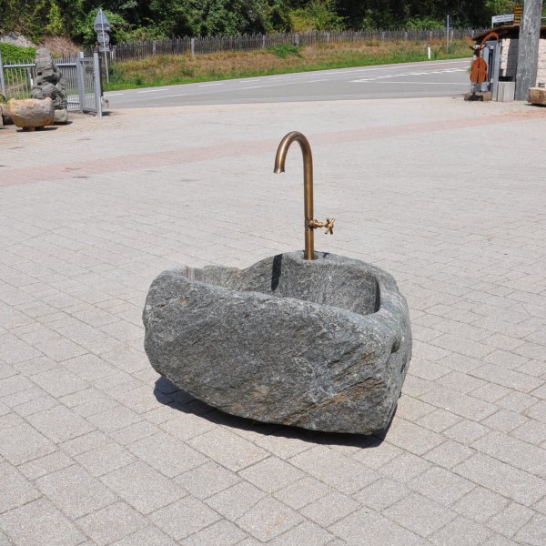 Natursteinbrunnen aus einem ausgehöhlten Granit-Findling als rustikale Wasserstelle im Garten