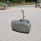 Natursteinbrunnen aus einem ausgehöhlten Granit-Findling als rustikale Wasserstelle im Garten